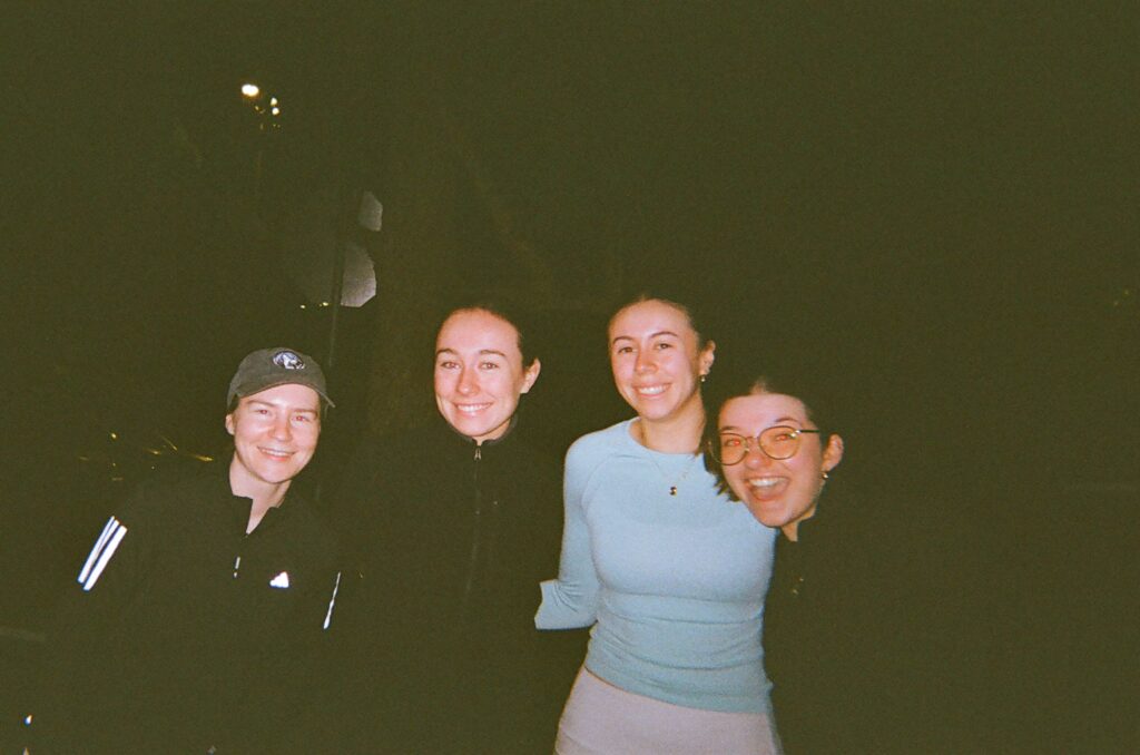 Four runners smiling together at night after a club run