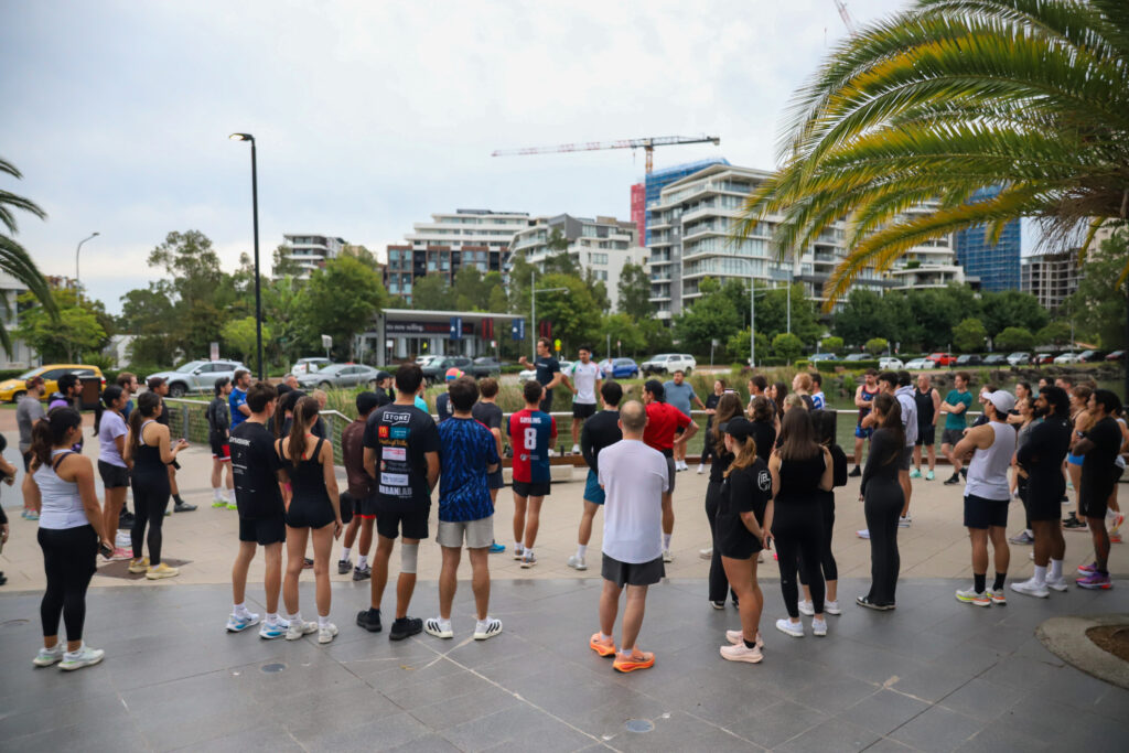 Runners gathered in a circle on an outdoor plaza, listening to a briefing before a run