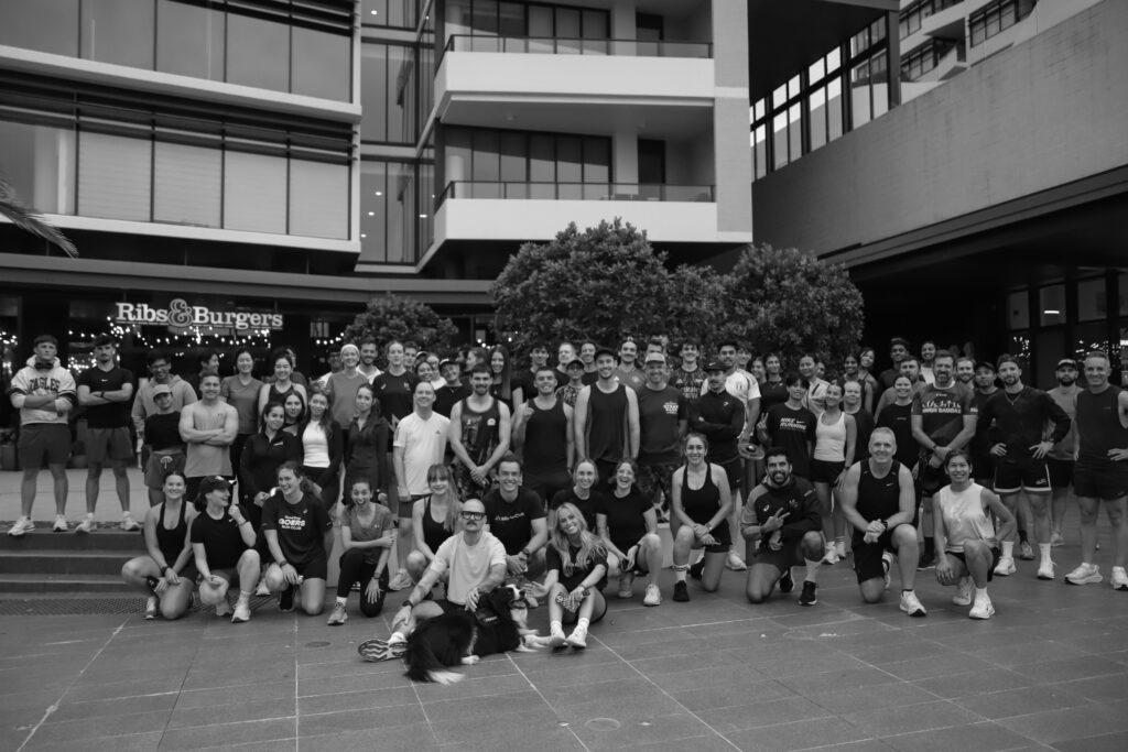 A large group of runners posing together outside a building in the evening