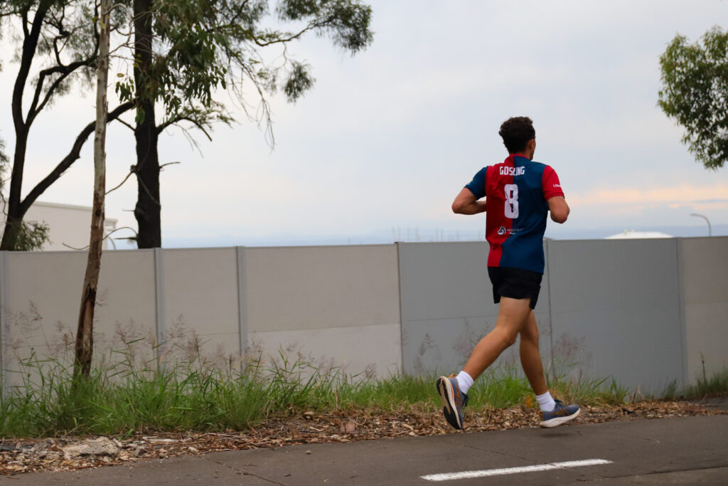 A runner in a red and blue club singlet running alone along a quiet path
