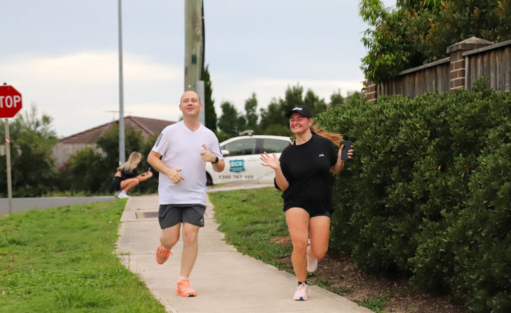 Two runners on a footpath, one of them smiling and waving at the camera during a club run
