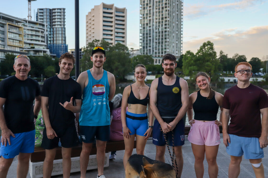 Seven Hills Run Club members in running gear posing together on a waterfront boardwalk with high-rise towers behind them