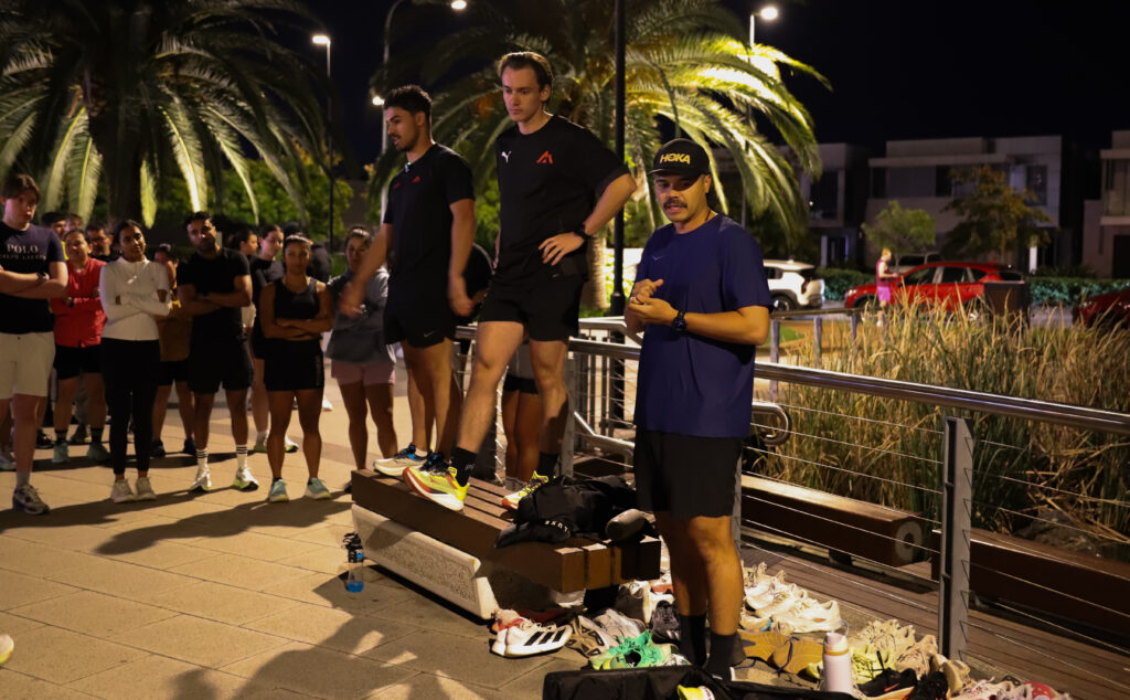 Runners gathered under the lights listening to the pre run briefing at a Hills Run Club night run