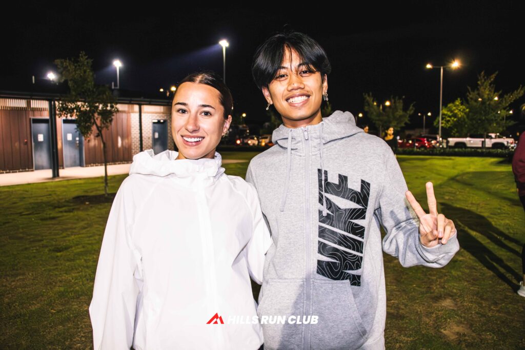 A woman in a white running jacket smiling at a night run under the lights