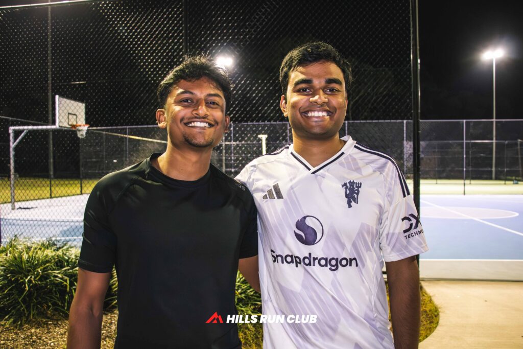 Two runners smiling together at a Hills Run Club night run under the lights