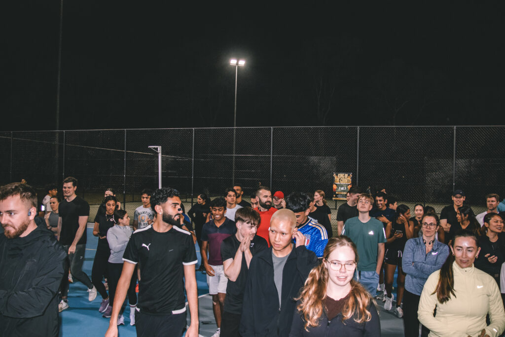 A large group of Hills Run Club runners gathered on a lit court at night