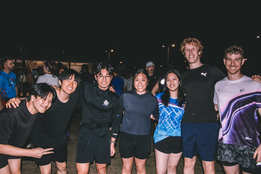 A group of seven runners smiling together after a Hills Run Club night run