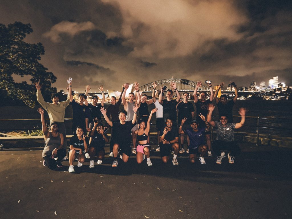 Hills Run Club runners together at night on Sydney Harbour with the Harbour Bridge behind them