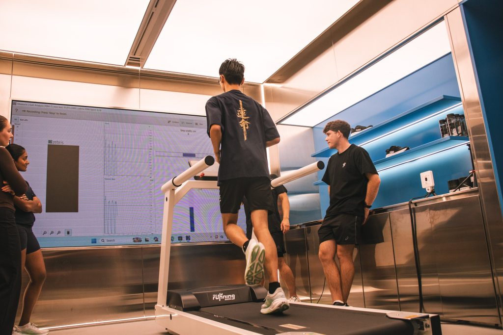 A runner on the HOKA Lab treadmill while others watch the screens